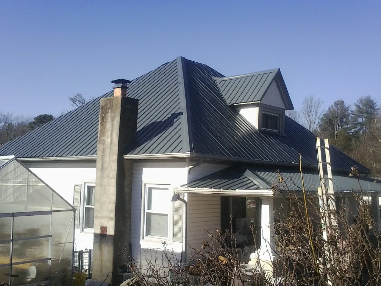 Dark blue standing seam metal roof on a white farmhouse with dormer — Slate & Tile Roof Repair by Roofing Brothers in Springport