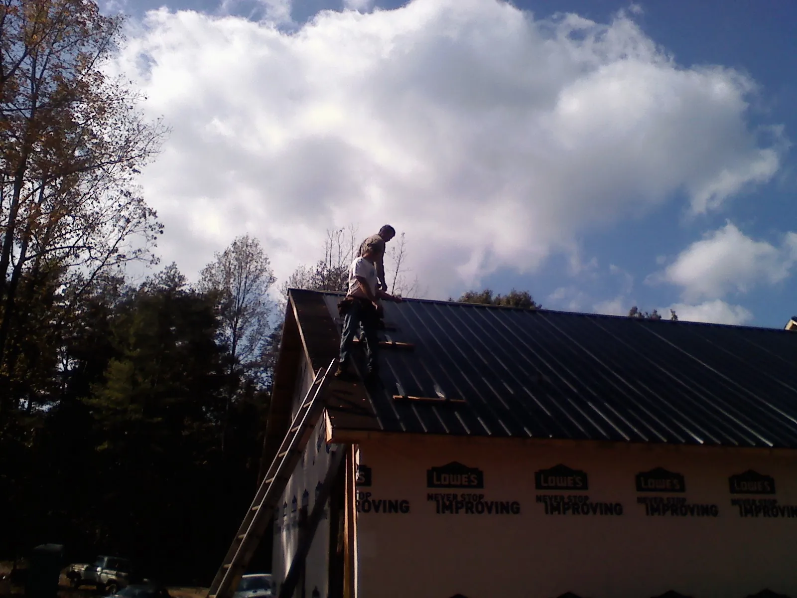 Roofer fastening dark metal panels high against a cloudy sky, from a Roof Inspection job in Springport