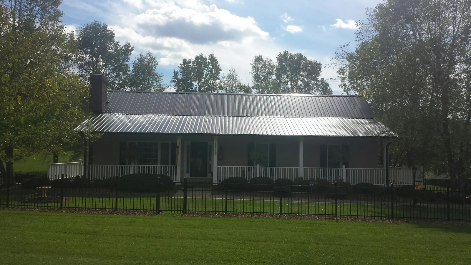 Gray metal roof on a brick ranch with a full width front porch — Gutter Guard Installation work by our crew in Springport