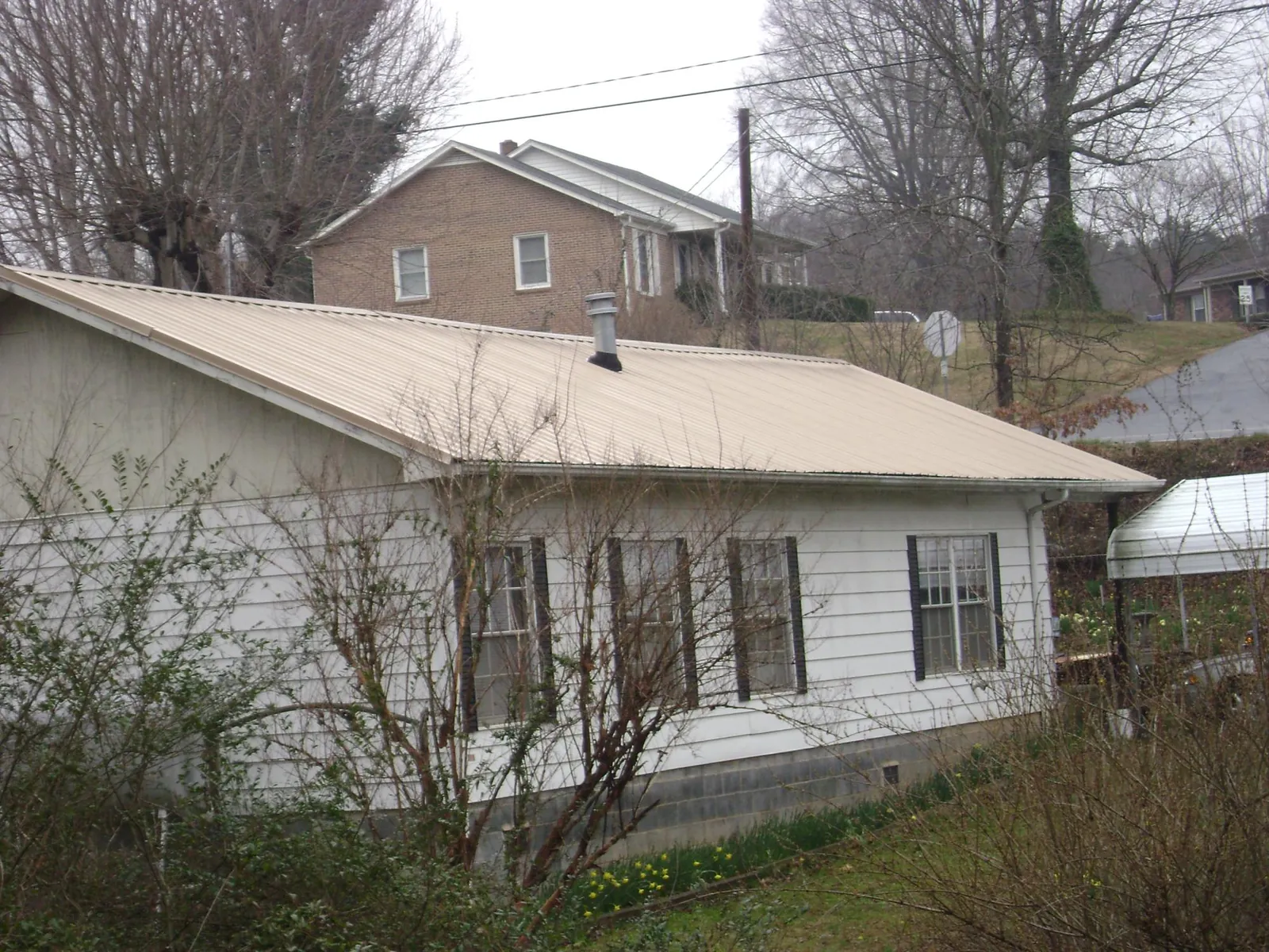 Tan metal roof on a white sided house set into a hillside — Commercial Roofing by Roofing Brothers in Springport